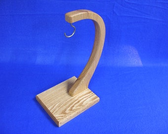 May include: A wooden stand with a curved arm and a metal hook. The stand is made of light brown wood with a natural grain pattern. The hook is made of silver metal and is attached to the top of the arm.