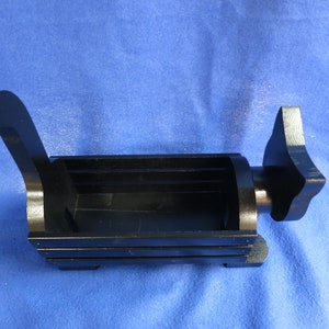 May include: A black, rectangular object with a handle and a star-shaped end. The object has a hollow interior and appears to be made of metal. The background is a solid blue color.