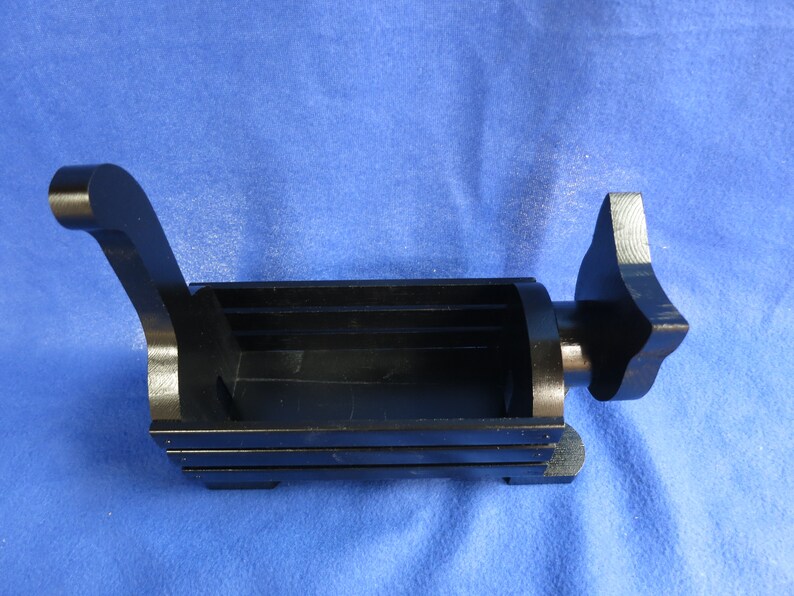 May include: A black, rectangular object with a handle and a star-shaped end. The object has a hollow interior and appears to be made of metal. The background is a solid blue color.
