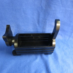 May include: A black wooden desk organizer shaped like a dog. The organizer has a rectangular compartment for storage, with a handle on the back and a dog head on the front. The dog-shaped organizer is on a blue surface.