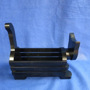 May include: A black wooden bench-shaped item, possibly a decorative piece or a small holder. The design features a slatted seat and curved back and armrests. The item is made of wood and painted black.