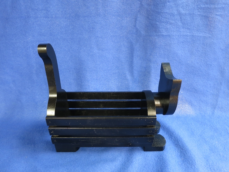 May include: A black wooden bench-shaped item, possibly a decorative piece or a small holder. The design features a slatted seat and curved back and armrests. The item is made of wood and painted black.