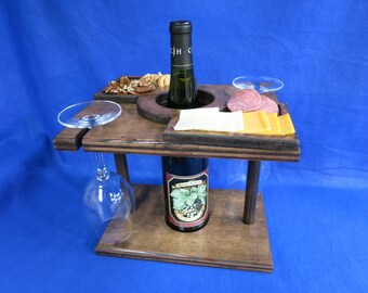 May include: Wooden wine and cheese serving stand with two glass goblets, a bottle of wine, cheese, salami, and nuts.