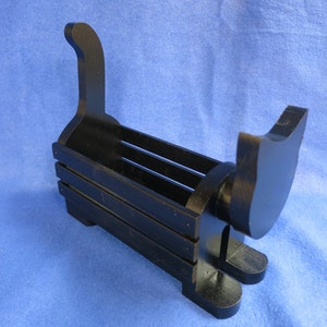 May include: A black wooden cat-shaped desk organizer. The organizer has a rectangular body with horizontal slats and a cat silhouette at each end. The cat's tail curves upwards. The organizer sits on two feet.