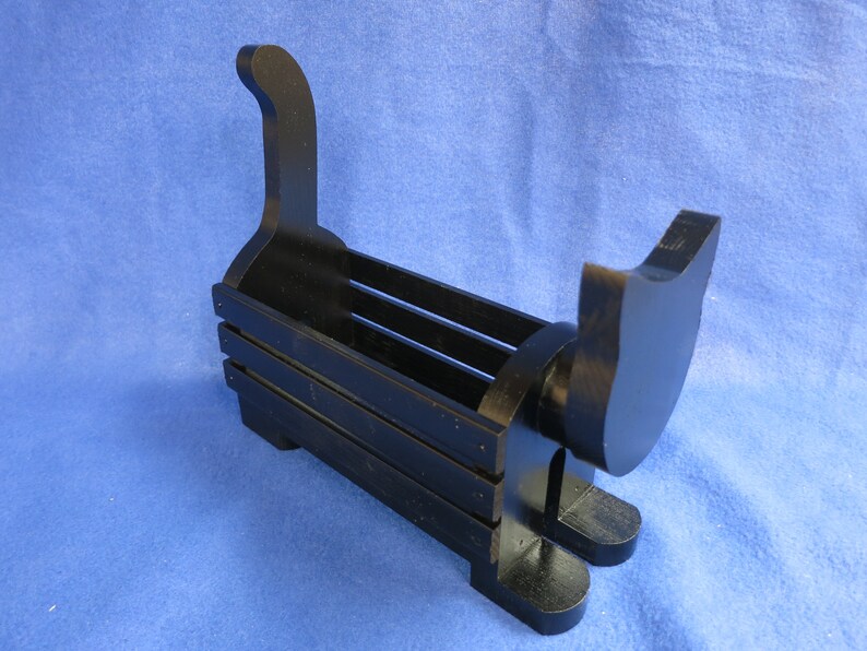 May include: A black wooden cat-shaped desk organizer. The organizer has a rectangular body with horizontal slats and a cat silhouette at each end. The cat's tail curves upwards. The organizer sits on two feet.