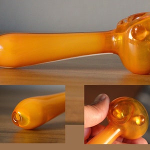 May include: A bright orange glass pipe with a rounded bowl. The pipe is made of thick glass and has a smooth finish.