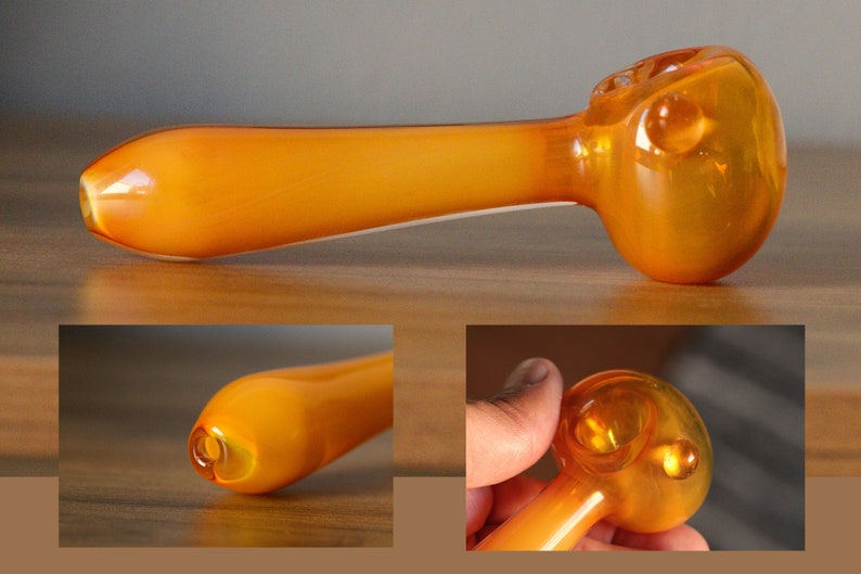 May include: A bright orange glass pipe with a rounded bowl. The pipe is made of thick glass and has a smooth finish.