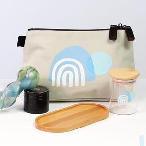 May include: A collection of accessories including a glass pipe, grinder, wooden tray, and a canvas pouch with a blue rainbow design. A glass jar with a wooden lid and a matching rainbow design is also included.