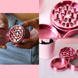 May include: A pink metal grinder with four pieces. The grinder has a top piece with a flower-shaped design, a middle piece with a screen, a bottom piece with a scraper, and a catch container.