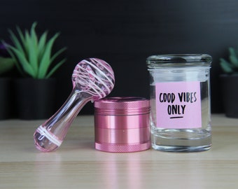 May include: Pink glass pipe with white swirl design, pink metal grinder, and a clear glass jar with a pink label that says "Good Vibes Only".