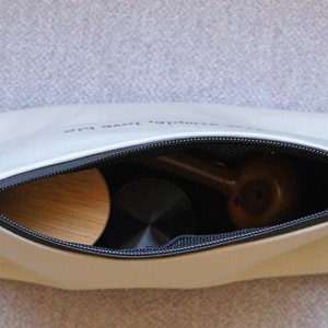 May include: A white zippered pouch with the text "simple love plus" printed on the front. The pouch is open and contains a wooden object, a black object, and a brown object.