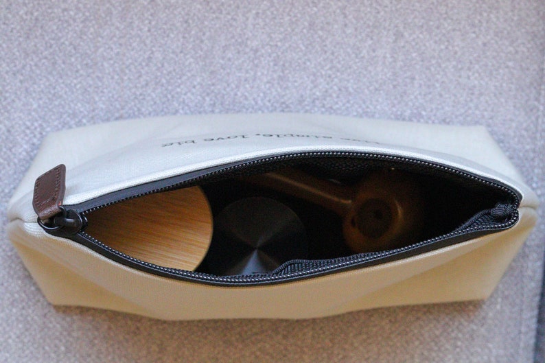 May include: A white zippered pouch with the text "simple love plus" printed on the front. The pouch is open and contains a wooden object, a black object, and a brown object.