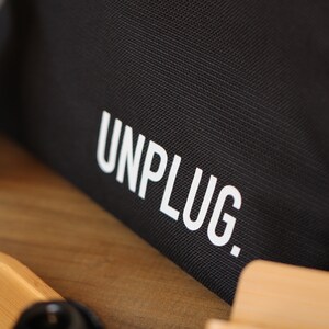 Może przedstawiać: Czarna torba z pł&oacute;tna z nadrukiem "UNPLUG." w kolorze białym.