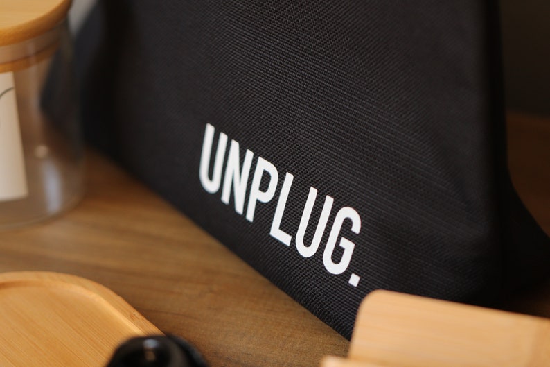 Może przedstawiać: Czarna torba z pł&oacute;tna z nadrukiem "UNPLUG." w kolorze białym.