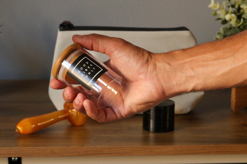 May include: A clear glass jar with a wooden lid and a black label that reads "GOOD VIBES ONLY".