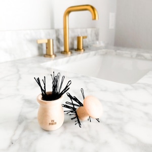 May include: A set of three ceramic mugs with a speckled, matte finish. The mugs are in shades of cream, light gray, and dark gray. Each mug has a simple, minimalist design and a rounded handle.