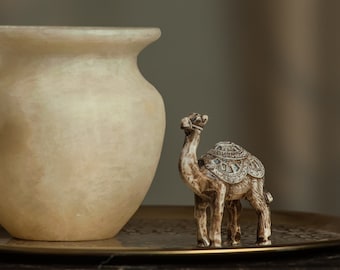 May include: A white alabaster vase and a small, detailed camel figurine are displayed on a gold tray atop a dark marble surface.