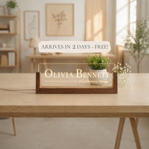 May include: A personalized desk nameplate with a wooden base and a clear acrylic panel. The name "Olivia Bennett" and the title "Client Relations Manager" are illuminated. The nameplate is on a wooden table.