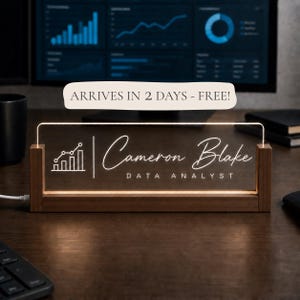 May include: A rectangular desk nameplate featuring a clear acrylic panel illuminated with white light, set in a dark wood base. The panel displays a line graph icon, the name Cameron Blake, and the job title DATA ANALYST in white lettering.