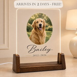 May include: A clear acrylic plaque with a light-up edge, featuring a circular photo of a golden retriever. Below the photo, the name "Bailey" is printed in black script, followed by the dates "2012-2026" in a simple font, set in a dark wood base.
