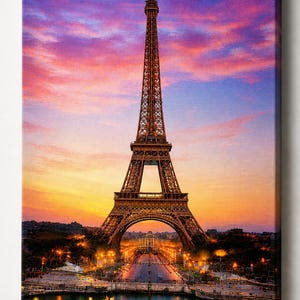May include: A canvas print of the Eiffel Tower in Paris at sunset. The iconic tower is brown, set against a vibrant sky of pink, orange, and blue hues. The Seine River reflects the city lights.