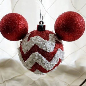 May include: Red and white Christmas ornament shaped like Mickey Mouse's head. The ornament has a red base with white zig-zag pattern and two red round ornaments for ears.