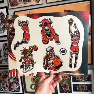 May include: A sheet of tattoo flash art featuring Chicago Bulls basketball imagery. The designs include illustrations of Michael Jordan in action and the team mascot, all in red, black, and white. The artist's name, @MINDINCHAINSTATTOOS, is printed at the bottom.