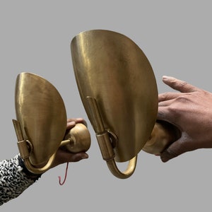 Op de afbeelding: Twee messing wandlampen met gebogen lampenkappen. De lampen hebben de vorm van een halve cirkel en een eenvoudig, elegant ontwerp.