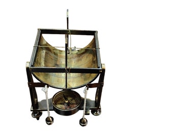 Könnte beinhalten: Eine Sonnenuhr aus Messing mit einem Kompass auf einem schwarzen Metallständer. Die Sonnenuhr hat ein gewölbtes Zifferblatt mit Markierungen und einem Zeiger. Der Kompass hat ein schwarzes Zifferblatt mit weißen Markierungen.