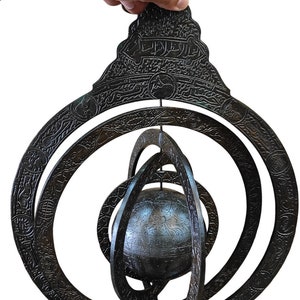 Puede incluir: Un globo celeste de metal negro con intrincados tallados y escritura árabe. El globo está suspendido dentro de una serie de anillos concéntricos, que representan las órbitas de los planetas.