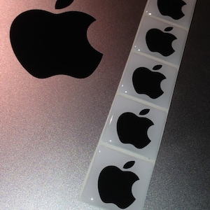 May include: Five silver stickers with black apple logos on a silver laptop. The stickers are arranged vertically in a row.