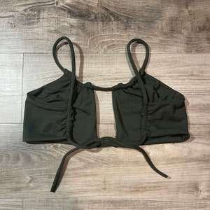 May include: Dark green crop top with thin straps and a keyhole design. The top features gathered fabric details on the sides and ties at the bottom. The top is made of a soft, stretchy material.