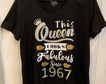 May include: Black v-neck t-shirt with a silver graphic that says "This Queen Looks Fabulous Since 1967". The graphic includes a crown and lips.