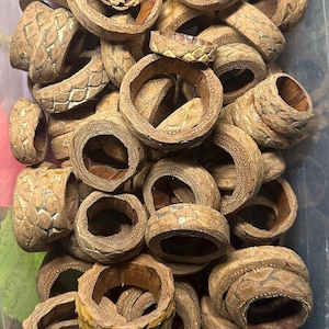 Peut inclure: Un ensemble de bagues en bois sculpté avec des motifs et des textures uniques. Les bagues sont de couleur marron chaud, avec des sculptures détaillées sur la surface extérieure. L'intérieur des bagues est lisse et de couleur plus claire. Les bagues sont de tailles variées.