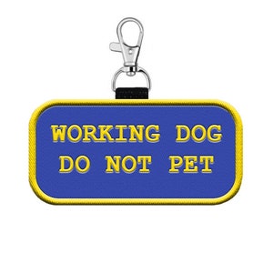 May include: Blue and yellow rectangular patch with the text "WORKING DOG DO NOT PET" attached to a silver clip.