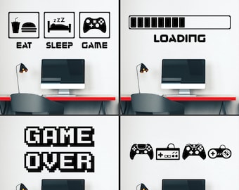 May include: Four black and white wall decals with a gaming theme. The decals include a progress bar with the word "LOADING", a set of three video game controllers, a pixelated "GAME OVER" sign, and a set of three icons that say "EAT", "SLEEP", and "GAME".