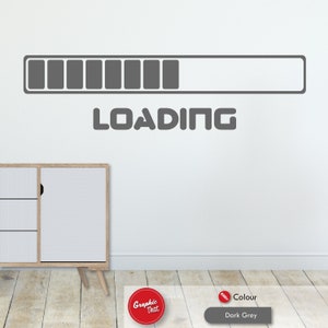 May include: Dark grey "LOADING" wall sticker featuring a progress bar design. The sticker is displayed on a white wall, with a modern cabinet visible in the lower left corner. The colour is dark grey.
