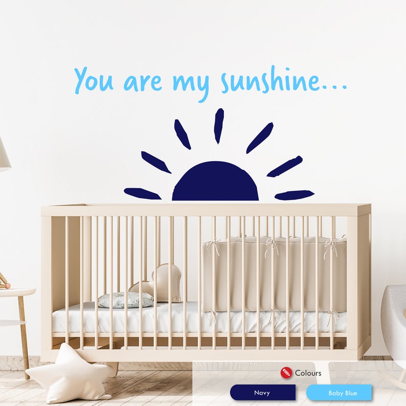 Peut inclure: Un autocollant mural de cr&egrave;che avec un soleil bleu et le texte "You are my sunshine..." en bleu clair. L'autocollant est plac&eacute; au-dessus d'un lit b&eacute;b&eacute; blanc avec un matelas blanc et une couverture blanche.