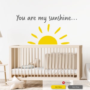 Peut inclure: Un autocollant mural de cr&egrave;che avec un soleil jaune et le texte "You are my sunshine..." en gris. L'autocollant est plac&eacute; au-dessus d'un berceau blanc avec un matelas blanc et une couverture blanche.