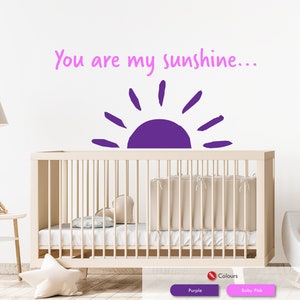 Peut inclure: Autocollant mural en vinyle violet avec le texte "You are my sunshine..." et un graphique de soleil violet. L'autocollant est affich&eacute; au-dessus d'un berceau blanc.