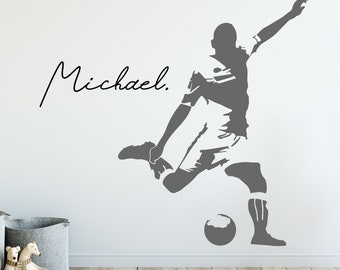 Puede incluir: Una silueta gris de un jugador de fútbol pateando un balón con el nombre "Michael" escrito en cursiva sobre el jugador. El jugador está pateando el balón con su pie derecho y su pierna izquierda está extendida detrás de él. El jugador lleva una camiseta de manga corta y pantalones cortos. El fondo es una pared blanca.