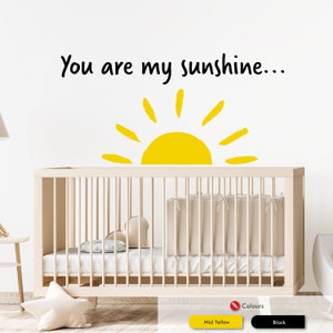 Peut inclure: Un mur blanc avec un autocollant noir et jaune qui dit "You are my sunshine..." avec un graphique de soleil jaune. Un lit b&eacute;b&eacute; blanc avec un matelas blanc et une couverture blanche est devant le mur.