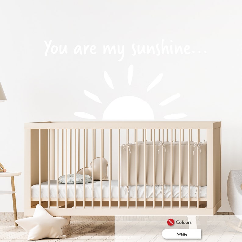 Peut inclure: Sticker mural blanc pour chambre d'enfant avec un soleil et le texte "You are my sunshine..." au-dessus d'un lit b&eacute;b&eacute; blanc avec un matelas blanc et une couverture blanche.