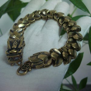 Op de afbeelding: Een gouden armband met een drakenkop sluiting en een ketting van overlappende schubben.