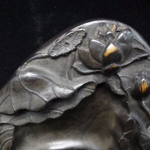 May include: Close-up of a dark, possibly metal, decorative object with a lotus flower and leaf design. The lotus flower has a light-colored center, and the leaves are intricately detailed.