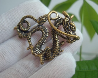 Puede incluir: Un colgante de metal dorado en forma de dragón con detalles intrincados. El dragón está enroscado con su cola en su boca, y sus alas están extendidas. El colgante es perfecto para agregar un toque de fantasía a cualquier colección de joyas.