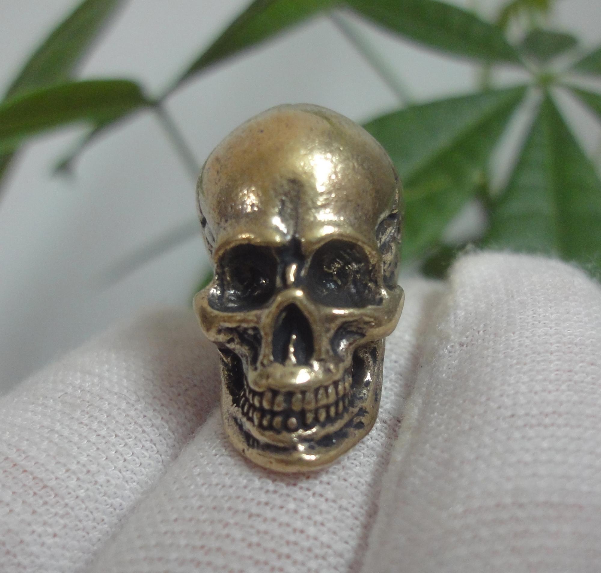 May include: A detailed gold-coloured metal skull figurine. The skull has a smooth, shiny finish and intricate details on the face.