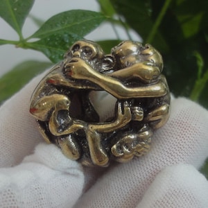 May include: A gold-colored metal sculpture of three monkeys intertwined. The monkeys are in a playful pose, with their arms and legs wrapped around each other.