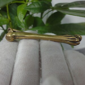 May include: A gold-colored metal charm shaped like a dog's leg with a paw at the end.
