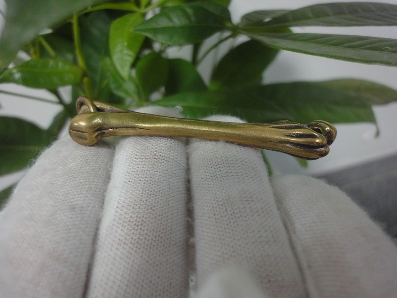 May include: A gold-colored metal charm shaped like a dog's leg with a paw at the end.